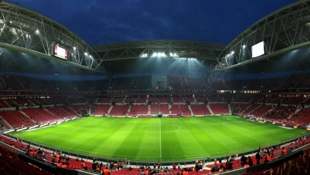 A panoramic view of a stadium illuminated at night, featuring green grass and empty red seats, set as an HD PC desktop wallpaper for sports enthusiasts.