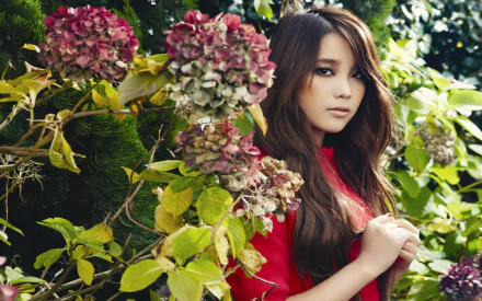 HD desktop wallpaper featuring an Asian woman in a red dress standing among vibrant hydrangeas and lush green foliage.
