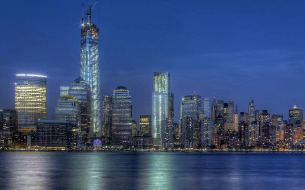 HD desktop wallpaper of New York's Manhattan skyline at dusk, a man-made panorama with One World Trade Center towering above the waterfront, lights reflecting on the water.