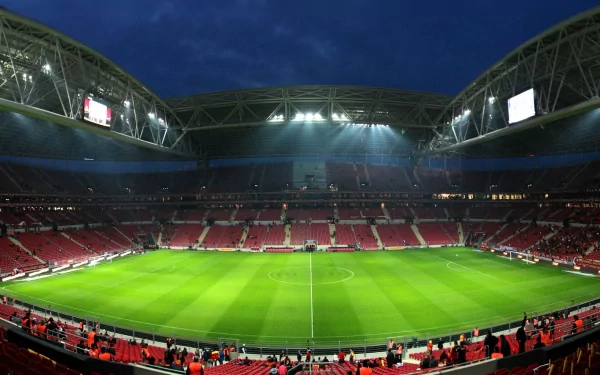 A panoramic view of a stadium illuminated at night, featuring green grass and empty red seats, set as an HD PC desktop wallpaper for sports enthusiasts.
