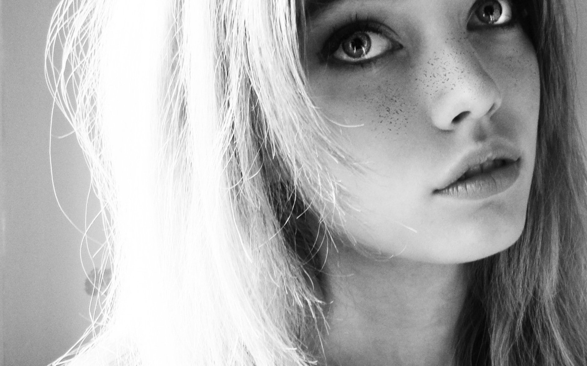 A close-up black and white image of a woman with striking eyes and freckles, showcasing her model features; an engaging HD wallpaper for desktops.