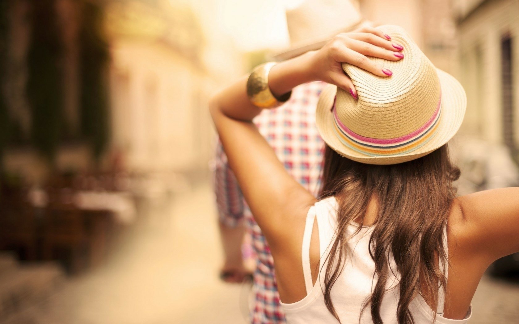 HD PC desktop wallpaper showing the rear view of a woman wearing a hat and holding it with both hands in a sunlit outdoor setting.