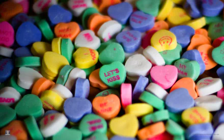 A vibrant close-up of colorful candy hearts in various pastel shades, featuring playful messages. This HD desktop wallpaper adds a sweet touch to your PC background.