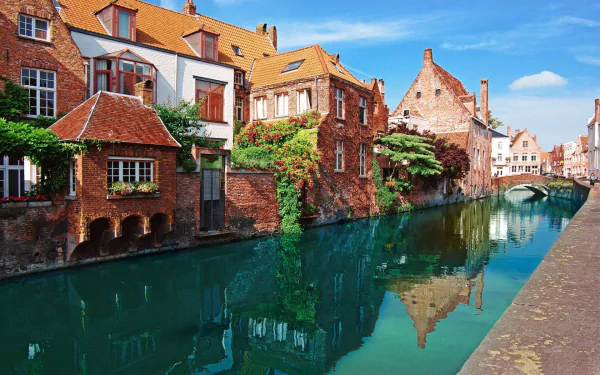 HD desktop wallpaper featuring man-made historic brick buildings along a calm canal in Bruges under a bright blue sky.