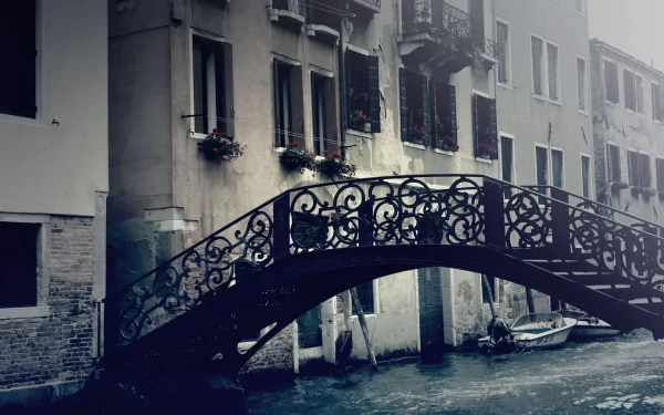 HD PC desktop wallpaper: moody Venice scene with a man-made ornate wrought-iron footbridge arching over a canal, weathered palazzi and a small boat drifting beneath.