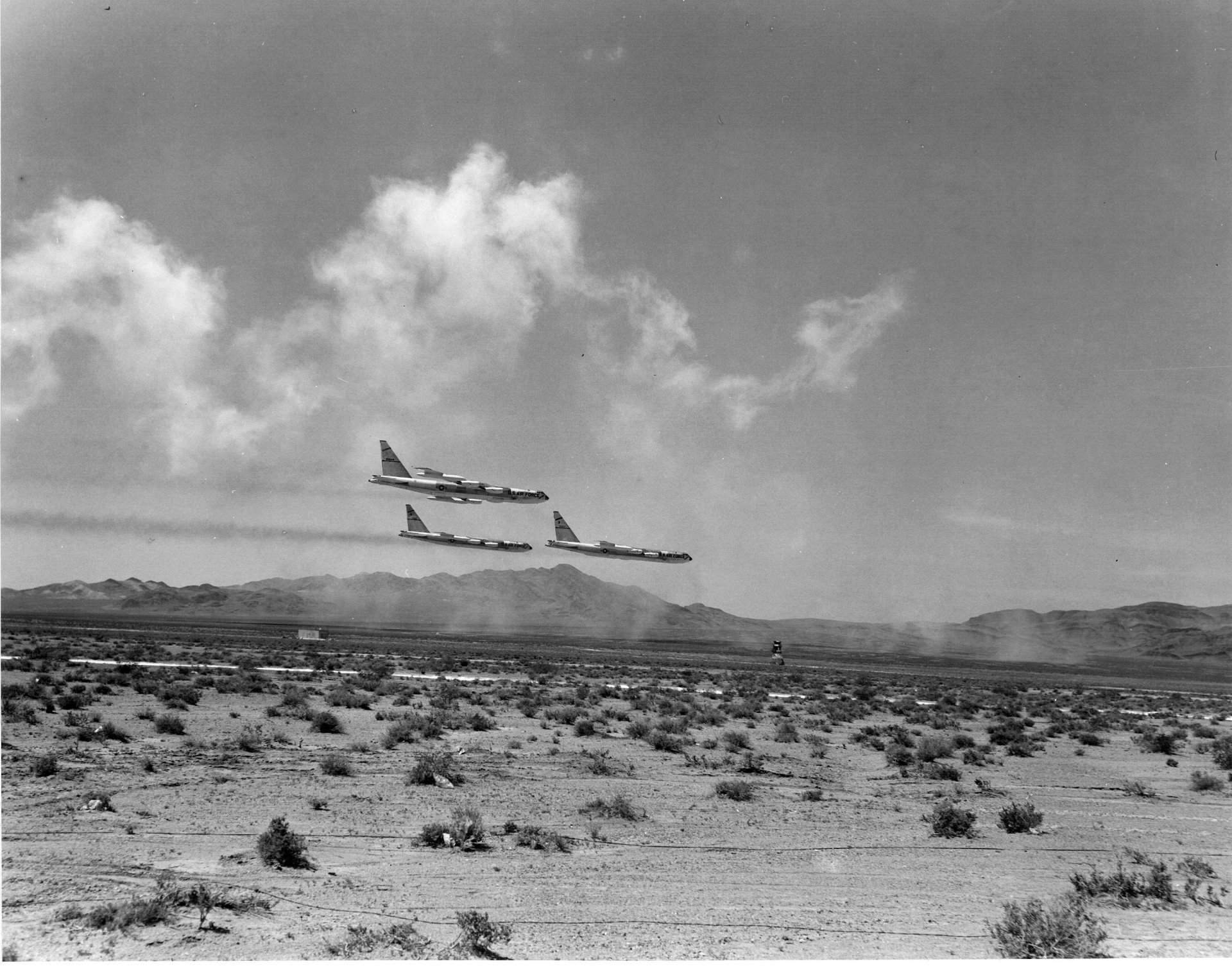 Black and white HD desktop wallpaper showing four Douglas DC-5 military aircraft flying in formation over a desert landscape.