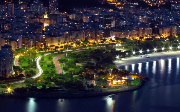 Nighttime aerial view of a man-made waterfront park in Rio de Janeiro, illuminated city buildings, and winding roads creating a vibrant HD desktop wallpaper background.