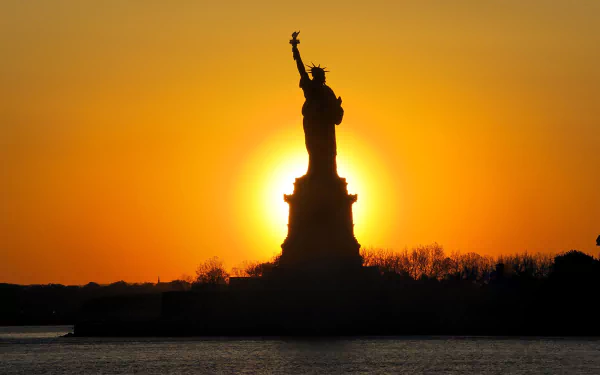 HD PC desktop wallpaper showing the Statue of Liberty silhouetted against a vibrant orange sunset sky.