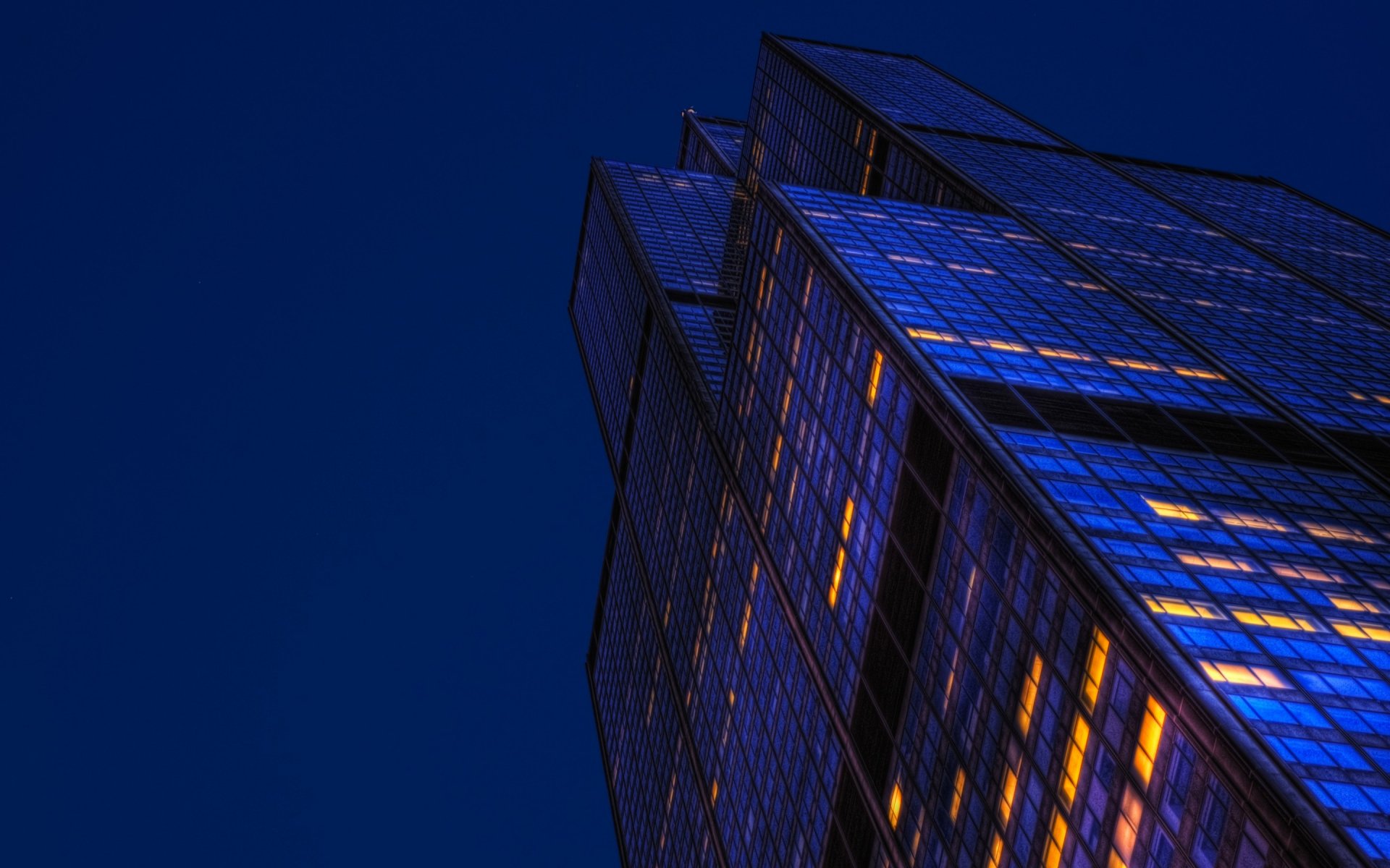 HD desktop wallpaper of a man-made skyscraper lit with warm lights against a deep blue night sky.