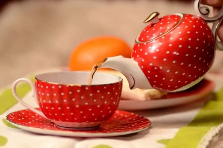 HD PC desktop wallpaper featuring a red polka-dot teapot pouring tea into a matching cup, accompanied by blurred food items in the background.