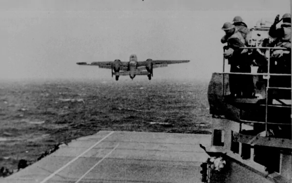 Black and white HD desktop wallpaper showing a North American B-25 Mitchell aircraft approaching an aircraft carrier deck with military personnel observing.