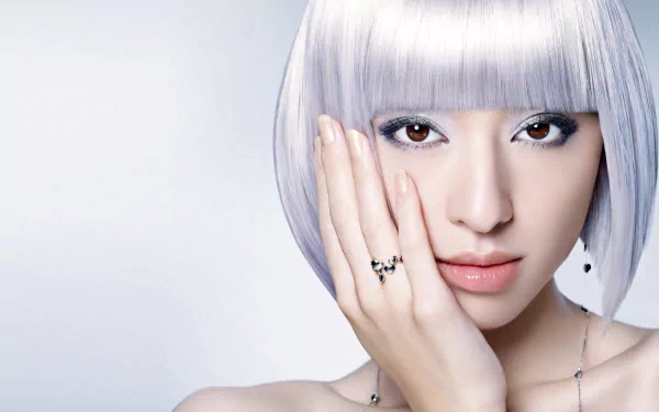A woman with a sleek silver bob hairstyle poses elegantly, showcasing her ring and a soft expression against a minimalist background. This HD wallpaper features a captivating aesthetic.
