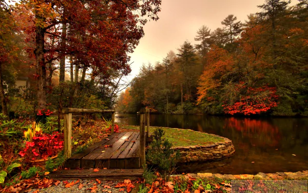 HD desktop wallpaper featuring a man-made wooden bridge over a calm river surrounded by vibrant autumn foliage.