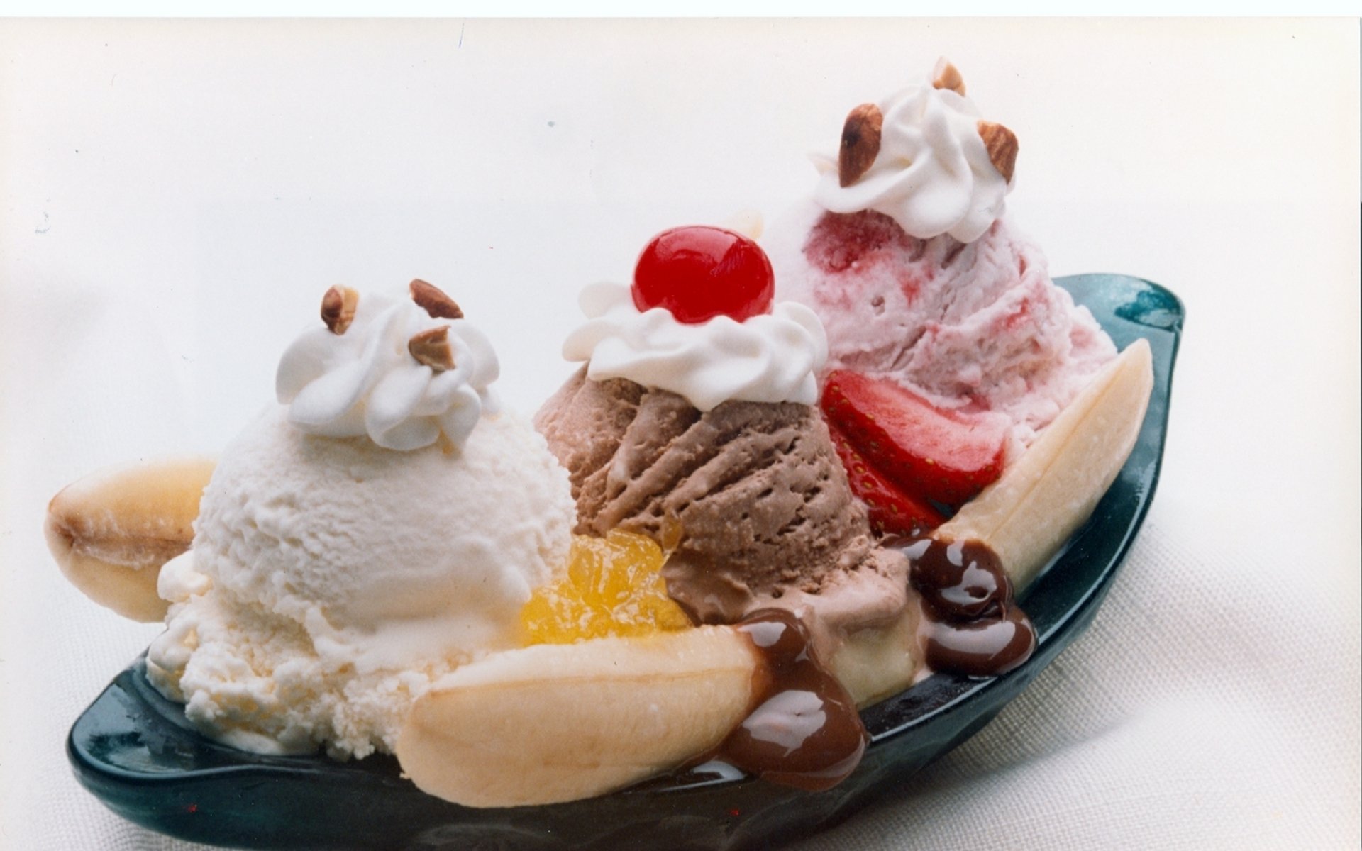 HD desktop wallpaper showcasing a classic banana split with scoops of vanilla, chocolate, and strawberry ice cream, topped with whipped cream, nuts, and a cherry.