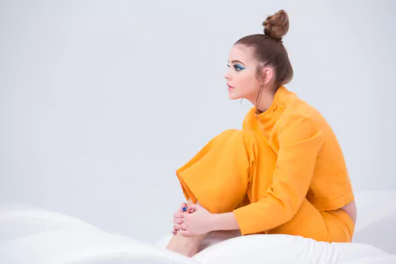 A stylish portrait of Hungarian celebrity Barbara Palvin, seated gracefully in a vibrant yellow outfit, exuding elegance and artistic flair against a minimalist backdrop.