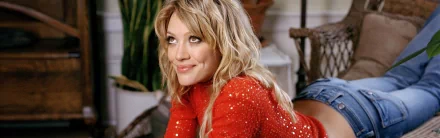 HD desktop wallpaper featuring celebrity Hilary Duff smiling with blonde hair, wearing a sparkling red top in a cozy indoor setting.