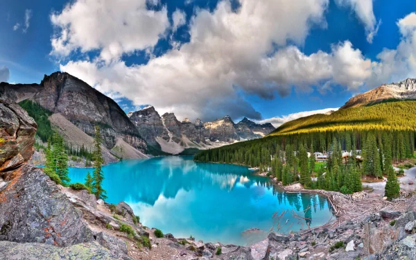 Stunning HD desktop wallpaper of Moraine Lake in Canada, showcasing crystal-clear turquoise water, surrounding pine forests, and majestic mountain peaks under a partly cloudy sky.