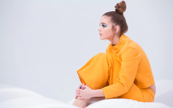 A stylish portrait of Hungarian celebrity Barbara Palvin, seated gracefully in a vibrant yellow outfit, exuding elegance and artistic flair against a minimalist backdrop.