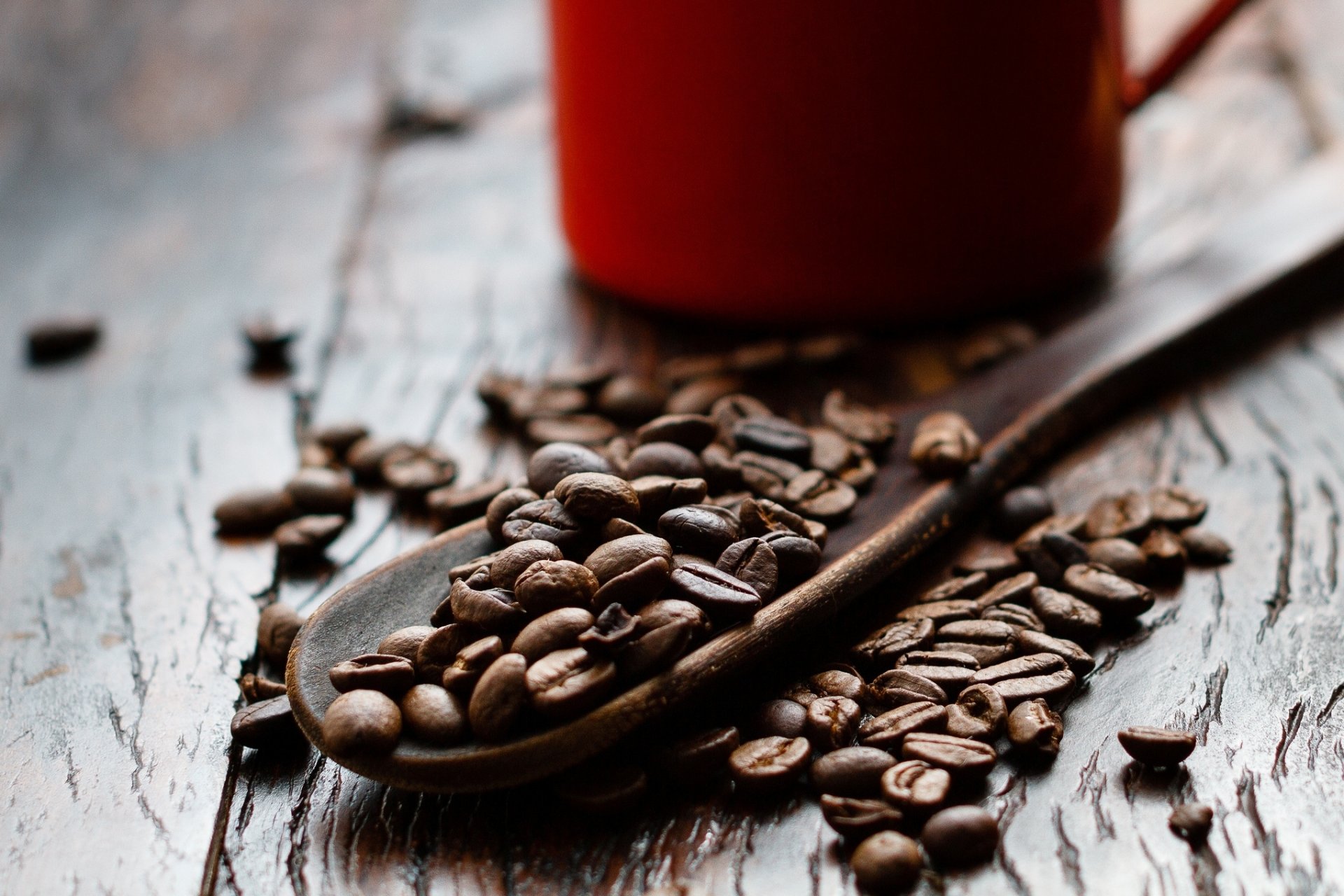 HD PC desktop wallpaper/background of coffee beans spilling from a wooden spoon on a rustic table with a red mug in soft focus (food, coffee)