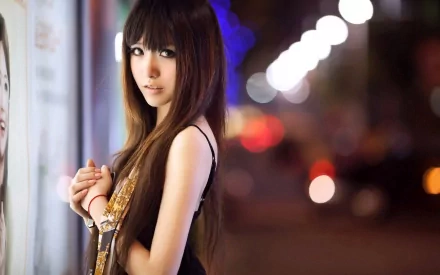 HD wallpaper featuring an Asian woman by a city street at night, highlighted by blurred lights in the background.