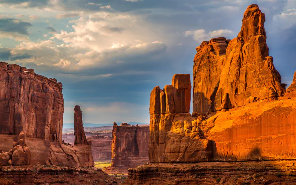 A stunning view of a canyon landscape, showcasing towering rock formations bathed in warm light under a dramatic sky. This captivating scene makes for a striking 4K Ultra HD desktop wallpaper.