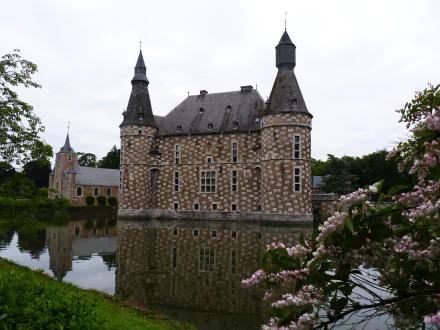 A picturesque view of Jehay-Bodegnée Castle reflecting in the serene waters, surrounded by lush greenery and blooming flowers, captured as an HD desktop wallpaper.