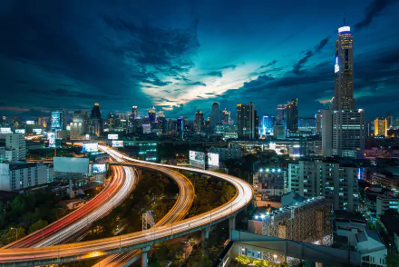 Time lapse view of Bangkok's cityscape at night with illuminated skyscrapers and light trails on curved highways, captured in HD for a vibrant PC desktop wallpaper.
