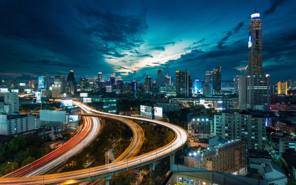 Time lapse view of Bangkok's cityscape at night with illuminated skyscrapers and light trails on curved highways, captured in HD for a vibrant PC desktop wallpaper.