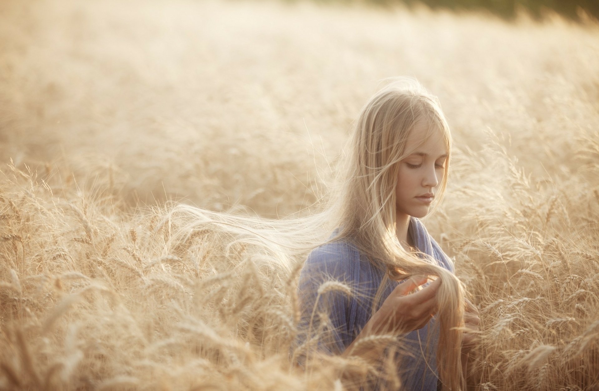 A serene woman stands in a golden field, gently holding her long hair as sunlight bathes the scene, creating a beautiful HD desktop wallpaper.