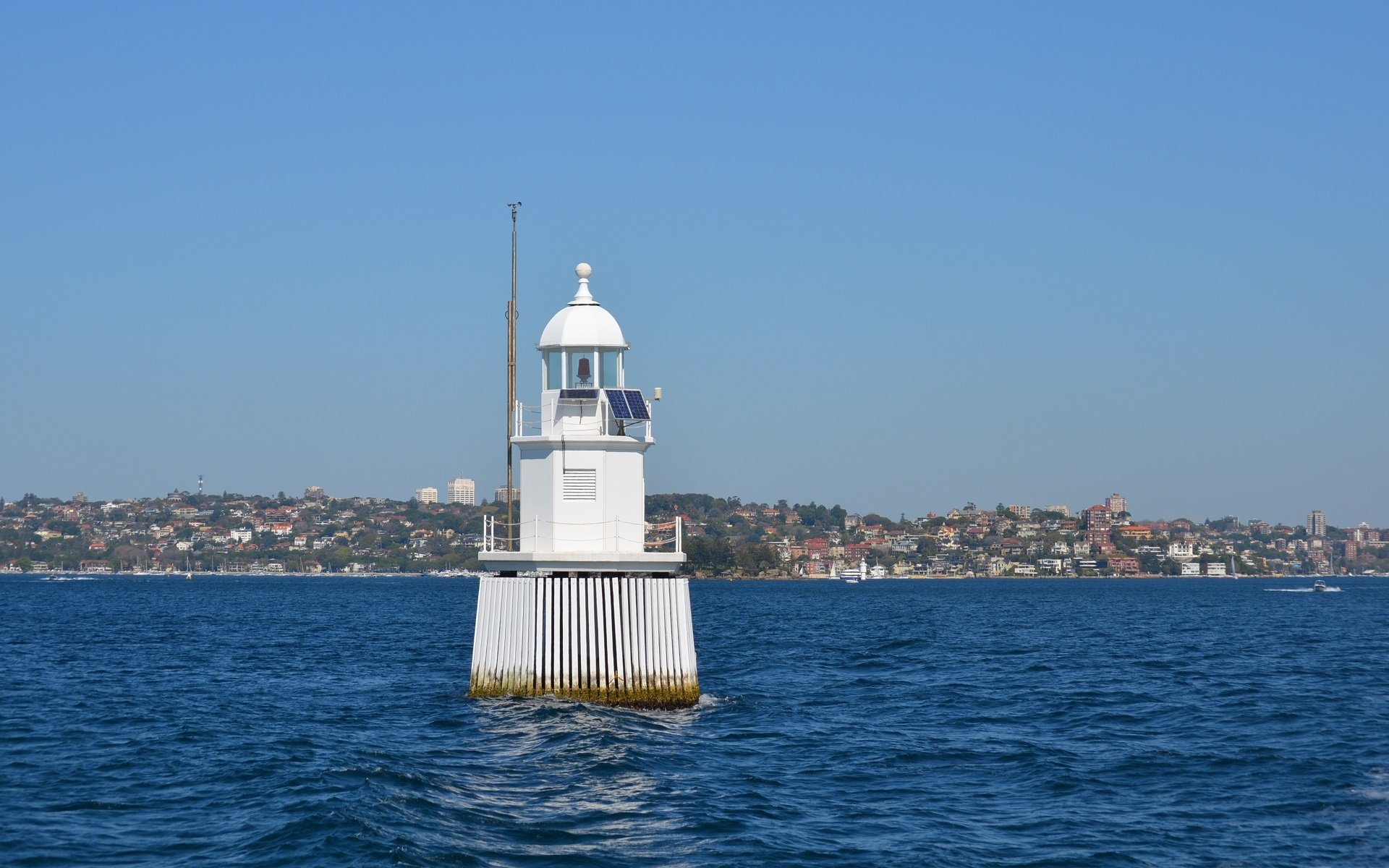 Man-made white buoy lighthouse stands in the blue waters of Sydney Harbour, Australia, against a clear sky and distant shoreline. HD desktop wallpaper.