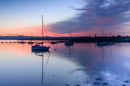 HD PC desktop wallpaper featuring a serene coastline with sailboats gently floating on calm waters under a vibrant sunset sky.
