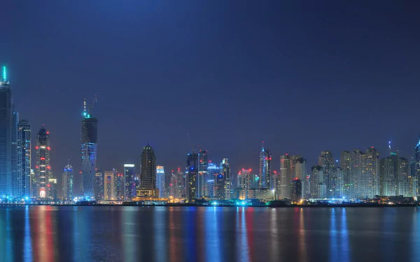 4K Ultra HD wallpaper showcasing the illuminated Dubai skyline at night with reflections on the water, capturing the city's iconic man-made architectural beauty.
