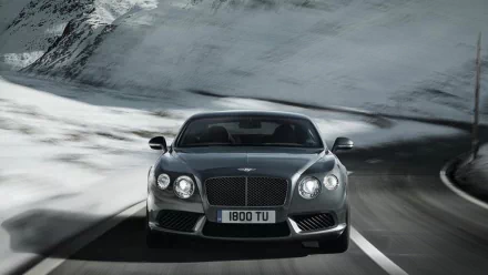 HD desktop wallpaper featuring a Bentley Continental GT Speed driving on a winding mountain road with snowy peaks in the background.
