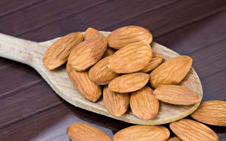 A close-up of almonds scattered on a wooden spoon, set against a dark wooden background, serves as a stylish HD desktop wallpaper and background.