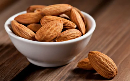 A close-up of a bowl filled with almonds, resting on a wooden surface. This high-definition image captures the natural beauty of food.