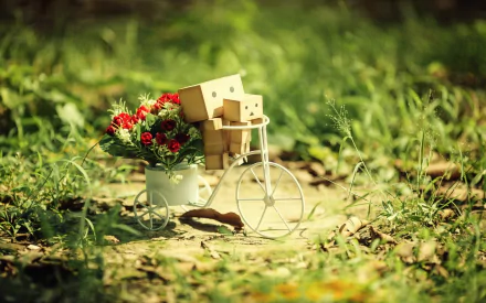 HD PC desktop wallpaper featuring a small danbo figure riding a miniature bicycle with a basket full of red flowers, set against a blurred natural background.