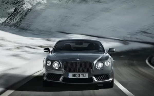 HD desktop wallpaper featuring a Bentley Continental GT Speed driving on a winding mountain road with snowy peaks in the background.