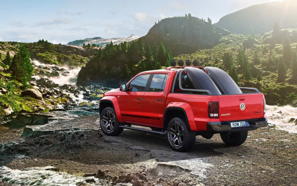 HD desktop wallpaper featuring a red Volkswagen Amarok parked on rugged terrain with mountains and a flowing river in the background.