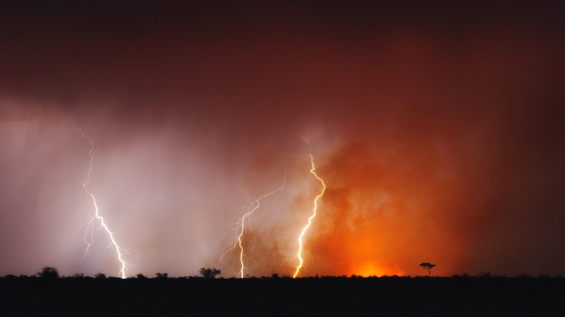 HD photography wallpaper capturing intense lightning strikes against a dark, smoky sky with an orange glow near the horizon.