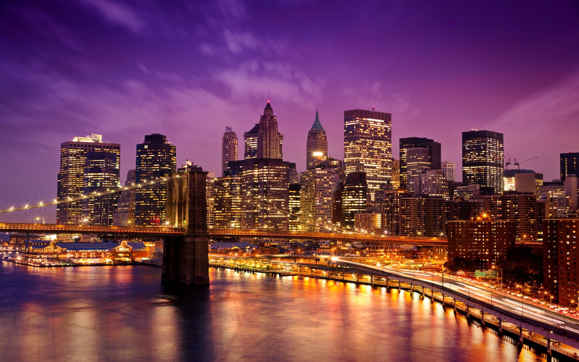 HD desktop wallpaper showcasing the illuminated Manhattan skyline at twilight with the Brooklyn Bridge in the foreground under a vibrant purple sky.