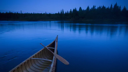 HD desktop wallpaper featuring a wooden canoe resting on calm blue water at dusk, with a forested shoreline in the background.