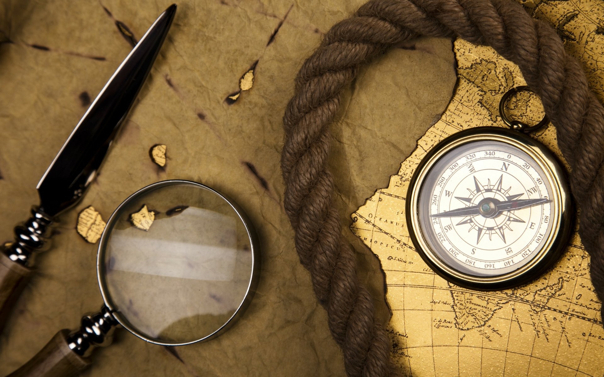 Vintage photography of a compass, magnifying glass, and rope on an aged map, captured in HD quality for a detailed PC desktop wallpaper and background.
