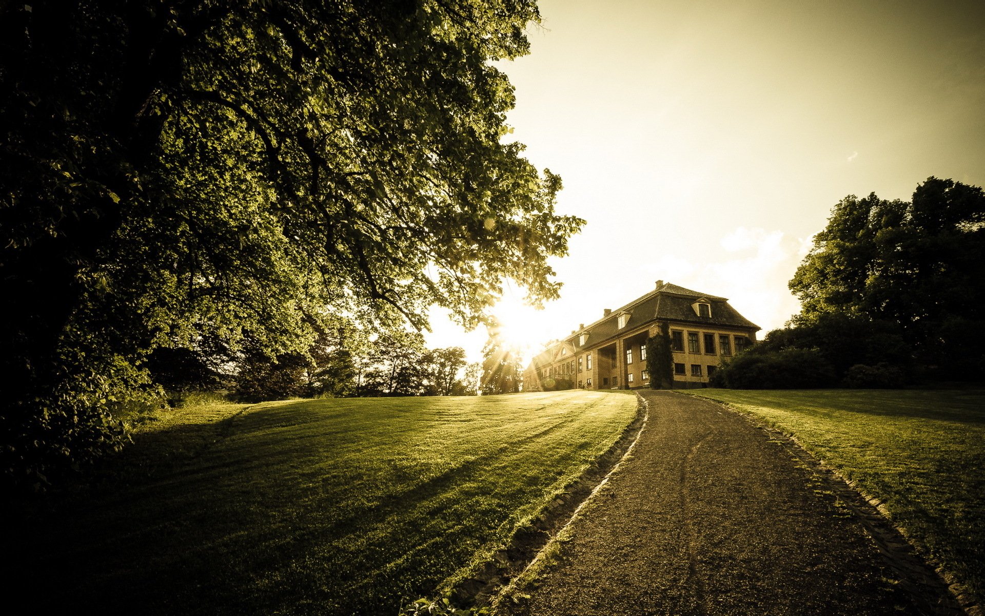 A scenic HD desktop wallpaper featuring a grand house bathed in warm sunlight, set against lush greenery and a winding pathway leading up to the entrance.