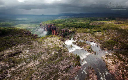Aerial view of Kakadu National Park showcasing rugged cliffs, lush greenery, and a flowing river under moody clouds, captured in HD for a nature-themed desktop wallpaper.