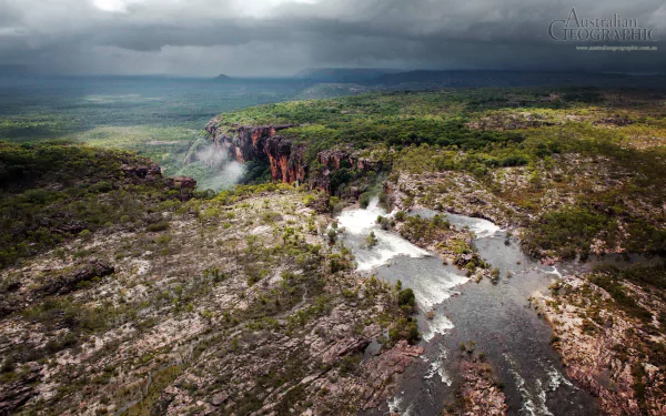 Aerial view of Kakadu National Park showcasing rugged cliffs, lush greenery, and a flowing river under moody clouds, captured in HD for a nature-themed desktop wallpaper.