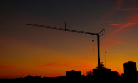 HD PC desktop wallpaper: silhouette of a man-made construction crane above a city skyline against an orange-purple sunset.