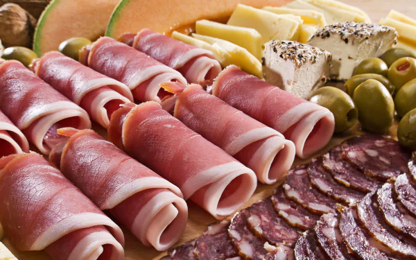 4K Ultra HD desktop wallpaper featuring a close-up of a charcuterie board with rolled cured meats, sliced salami, cheeses, olives, and melon slices.