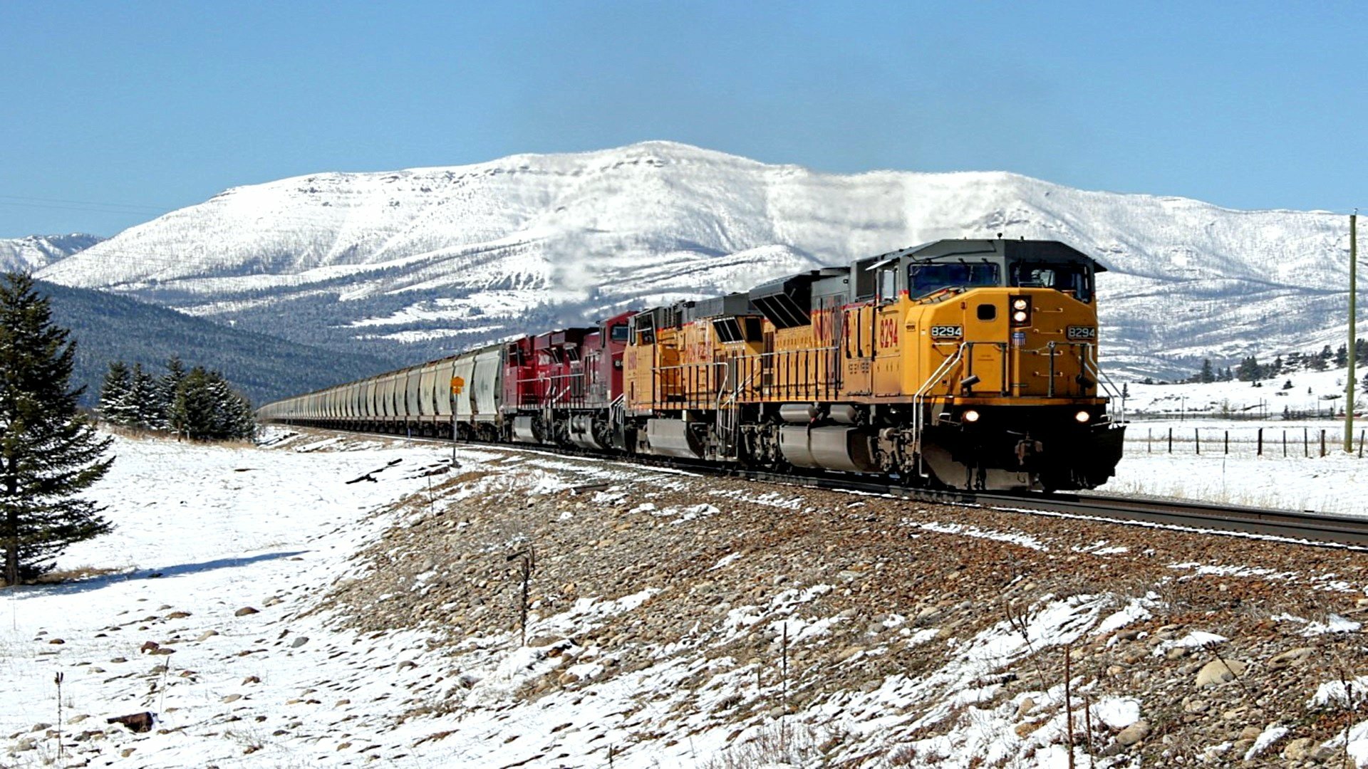 A powerful train travels through a snow-covered landscape, with mountains in the background, captured as an HD PC desktop wallpaper and background.