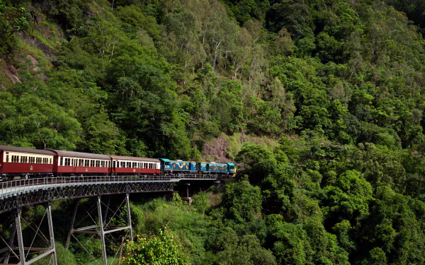 A vibrant train travels along a curved bridge, surrounded by lush greenery, creating a captivating HD desktop wallpaper and background.