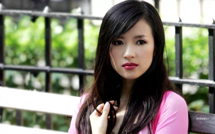 A captivating portrait of the celebrity Zhang Ziyi, featuring her in a pink top with lush greenery in the background, making for a striking HD desktop wallpaper.